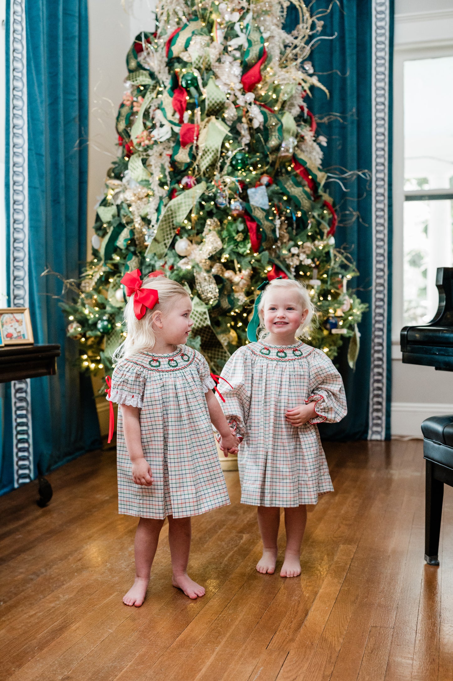 Two young girls in matching dresses standing in front of a decorated Christmas tree.