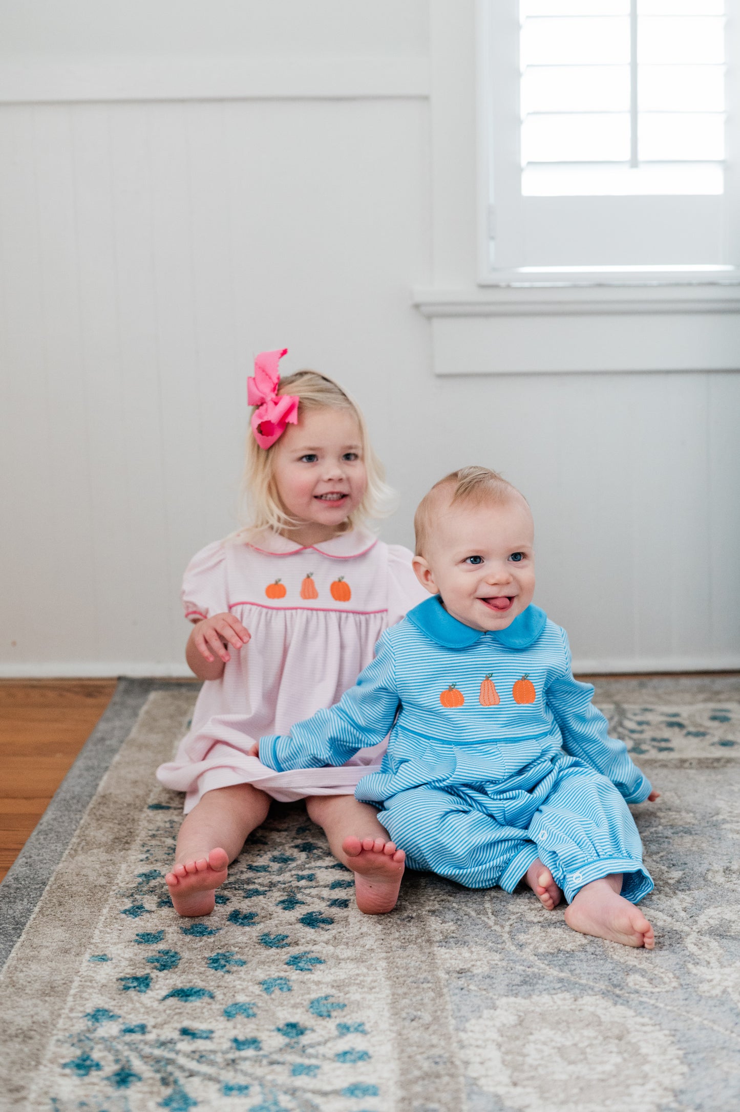 Two children sitting on a rug in a room with a window in the background