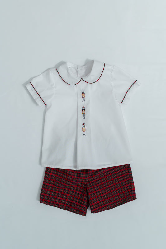 White shirt with red trim and plaid shorts on a light gray background