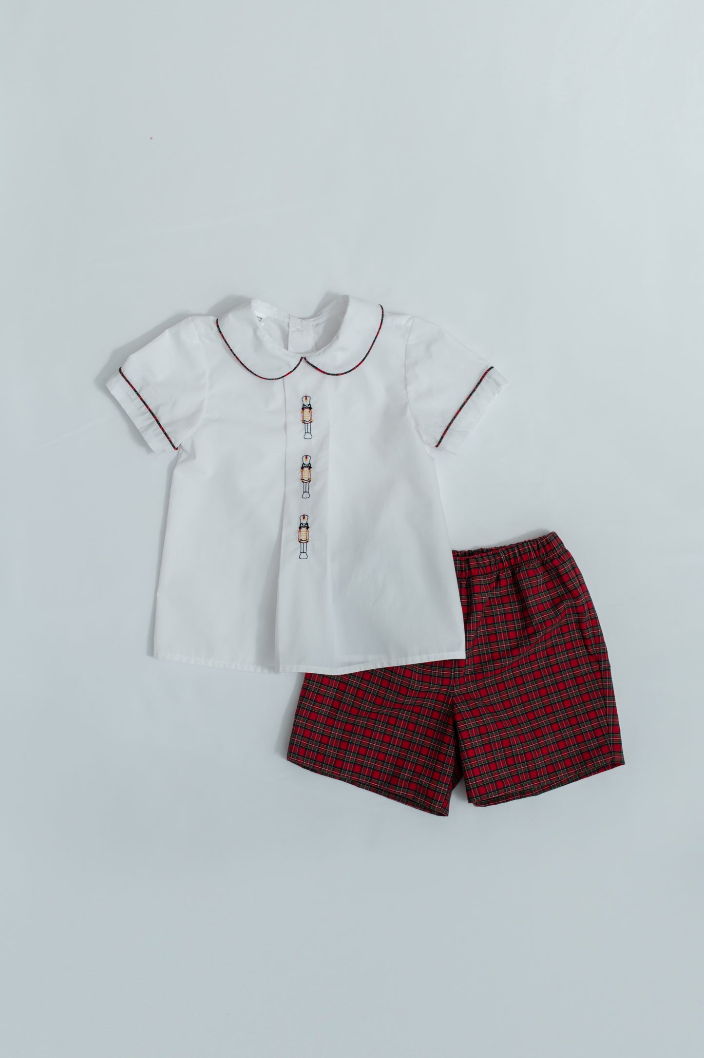White shirt with a collar and red plaid shorts on a light gray background