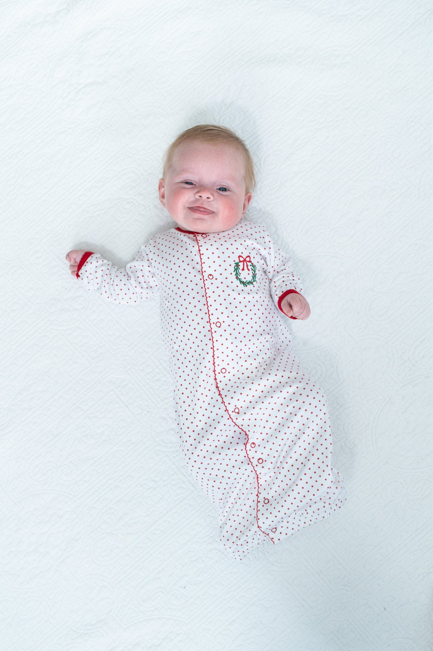 Baby in a white polka dot onesie with red trim lying on a white background