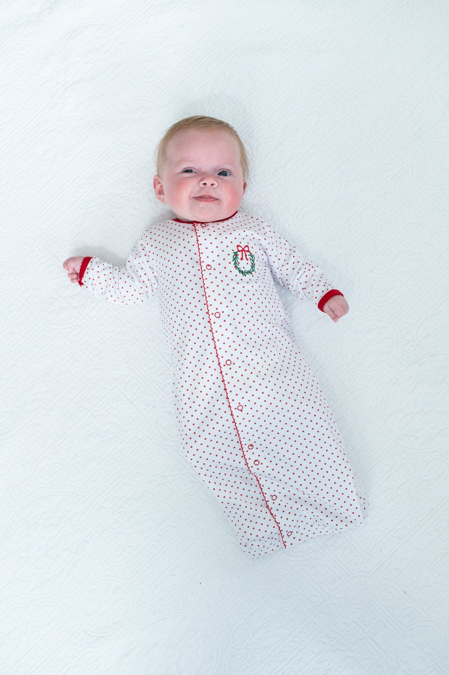 Baby lying on a white surface wearing a patterned onesie with red accents.