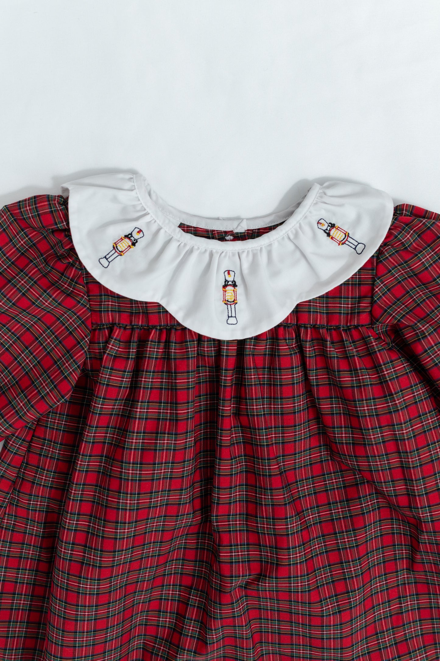 Red plaid dress with white collar featuring embroidered designs on a light gray background