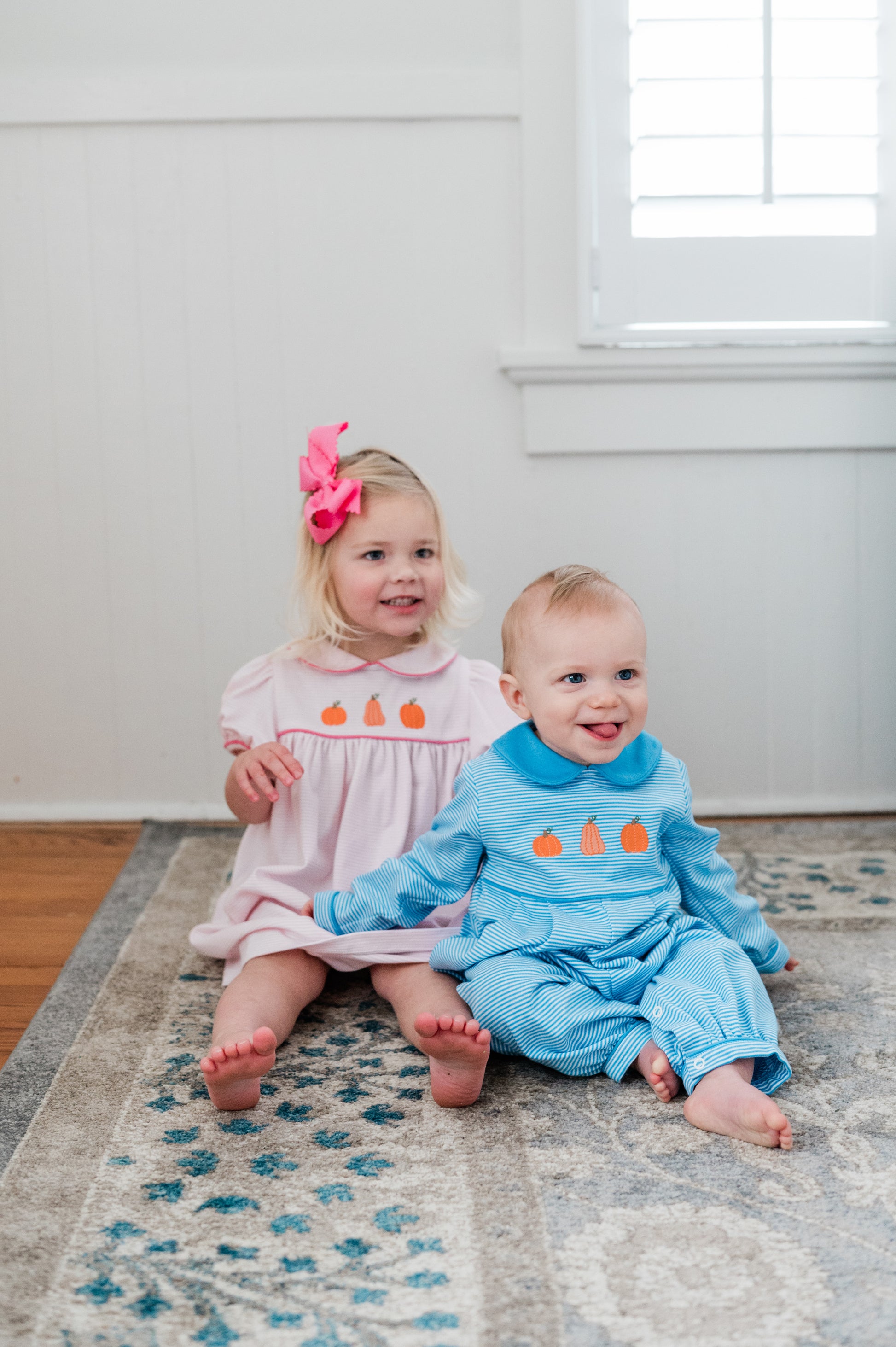 Two children sitting on a rug in a room with a window in the background
