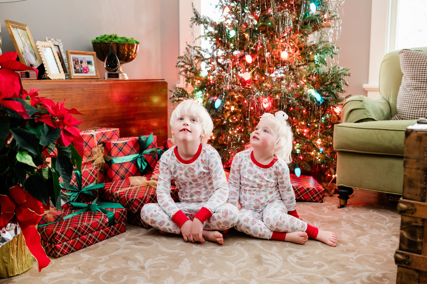 Two children in Christmas jammies sitting in front of a Christmas Tree