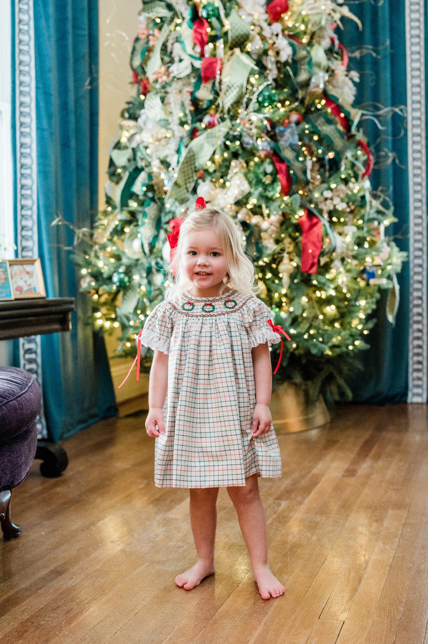Young girl in a plaid dress standing in front of a decorated Christmas tree.