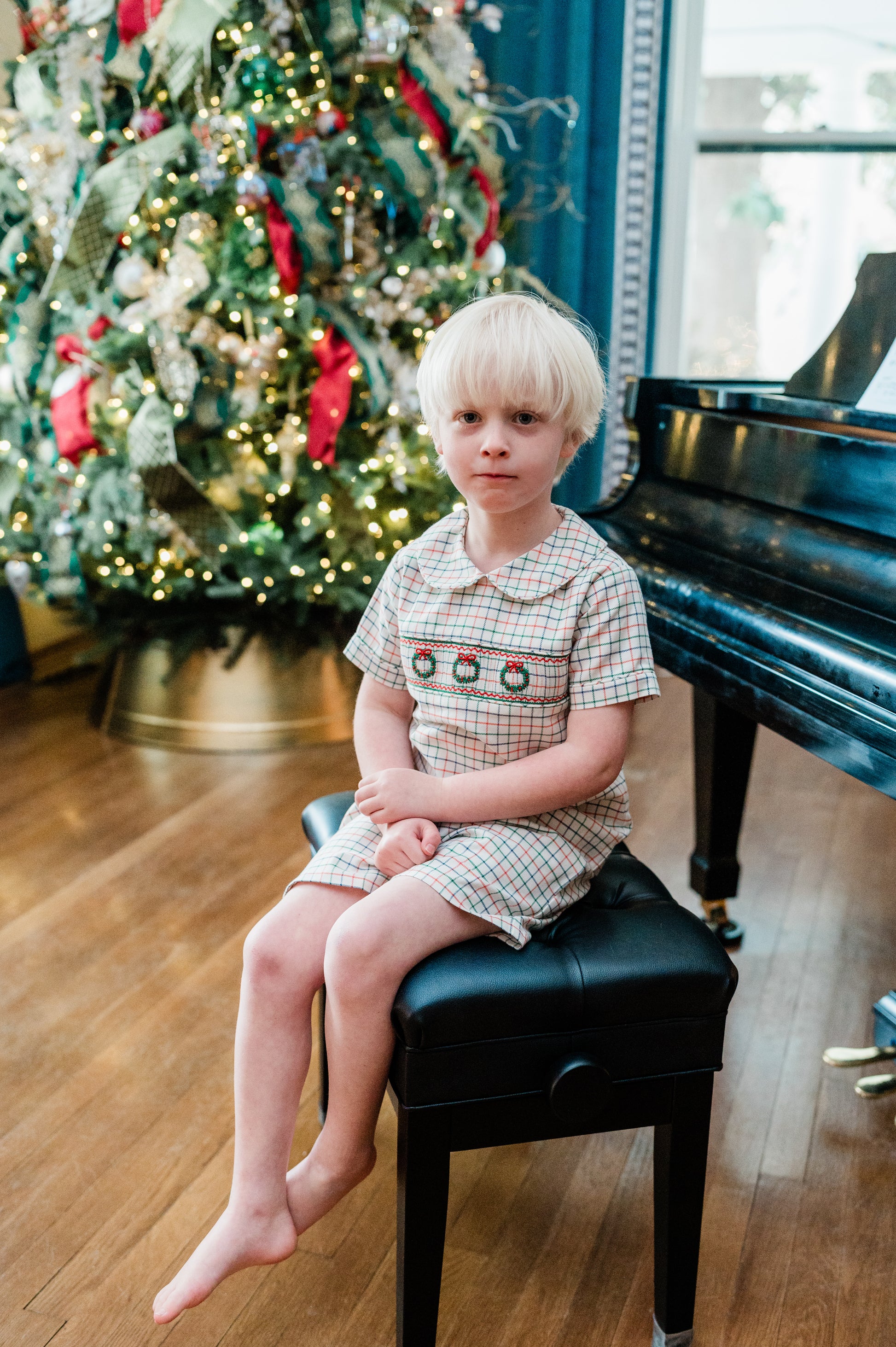 Child sitting on a piano bench in front of a decorated Christmas tree