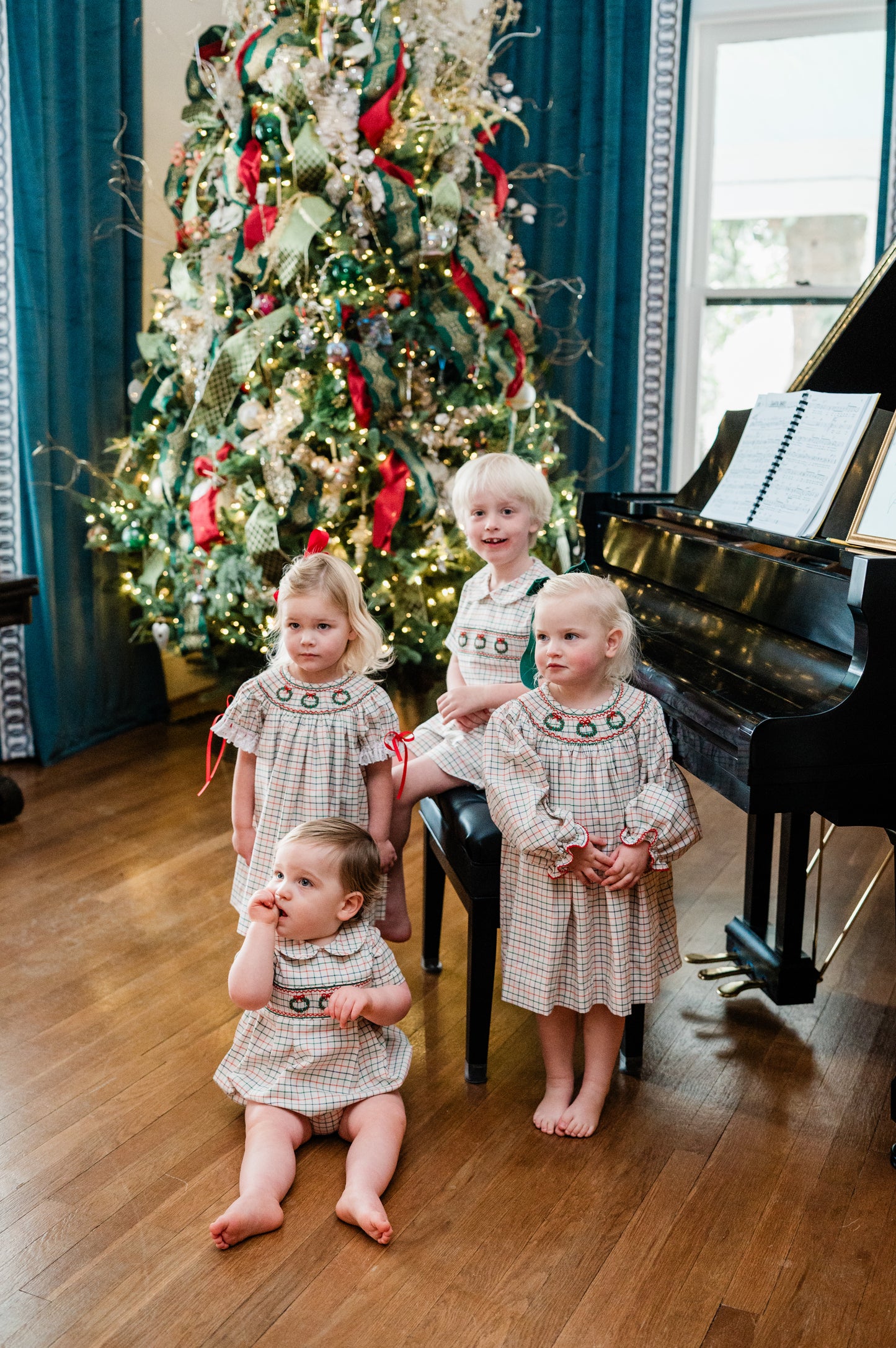 Children in matching dresses standing in front of a decorated Christmas tree and piano.