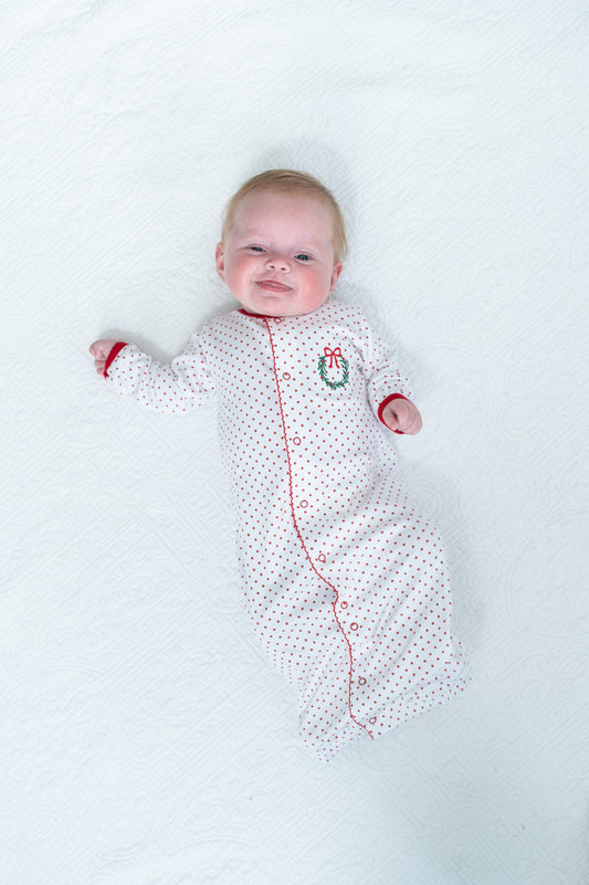 Baby in a white polka dot onesie with red trim lying on a white background
