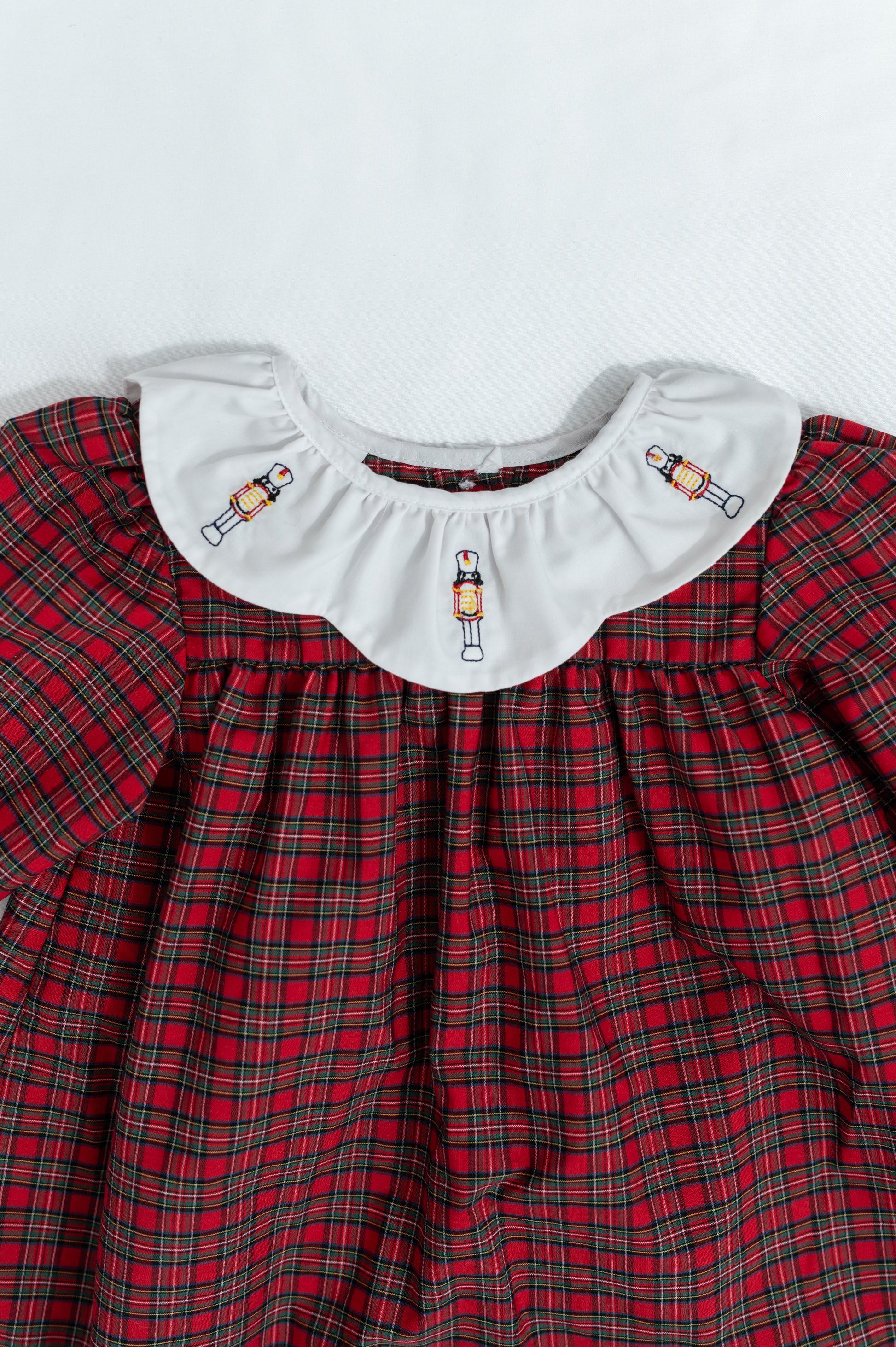 Red plaid dress with white collar featuring embroidered designs on a light gray background